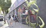 Se observa un mural de calavera y un grafitero pintando