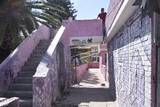 Se observa una casa con la fachada rosa, muy dañada y rota, escaleras viejas y rotas