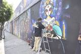 Se observa un mural de una catrina y un grafitero pintando