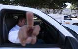 Se observa a un hombre dentro de un coche apuntando con el dedo medio de la mano hacía la cámara